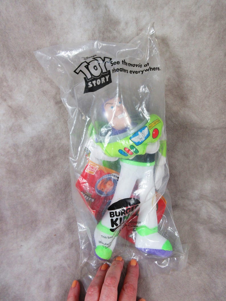K&ouml;nnte beinhalten: Eine Buzz Lightyear-Actionfigur aus dem Film "Toy Story" in einer durchsichtigen Plastikt&uuml;te. Die Figur ist wei&szlig;, gr&uuml;n und lila, mit dem Burger King-Logo auf der Verpackung. Die T&uuml;te hat auch das "Toy Story"-Logo.