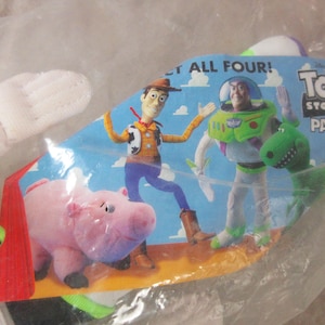 K&ouml;nnte beinhalten: Ein Toy Story Pals Spielzeugset mit den Charakteren Woody, Buzz Lightyear, Hamm und Rex. Die Verpackung ist blau mit den Worten "LET ALL FOUR!" und "Toy Story Pals". Das Spielzeug befindet sich in einer transparenten Plastikt&uuml;te.