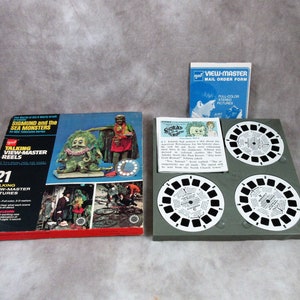 Puede incluir: Un conjunto de carretes View-Master vintage con los personajes Sigmund y los Monstruos Marinos. La caja es roja y blanca con una imagen de Sigmund y un monstruo marino. Los carretes están en una caja de plástico verde. El conjunto incluye 21 imágenes parlantes View-Master.