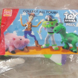 K&ouml;nnte beinhalten: Ein versiegelter Plastikbeutel mit einem Werbeartikel von Burger King. Der Artikel zeigt eine farbenfrohe Karte mit den Toy Story-Charakteren Woody, Buzz Lightyear, Rex und Hamm. Auf der Karte steht "ALLE VIER SAMMELN!" und "TOY STORY PALS".