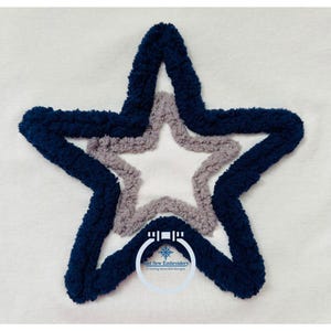 May include: A white fabric with a blue and gray embroidered star. The star is outlined in blue and has a smaller gray star inside. The text "Just Sew Embroidery" is in a circle below the star.