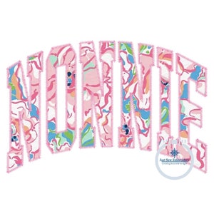 May include: A pink and white floral design with the name "NONNIE" in a large, bold font. The design is outlined in pink and has a stitched effect. The text "Just Sew Embroidery Creating Beautiful Designs" is in a smaller font at the bottom of the image.