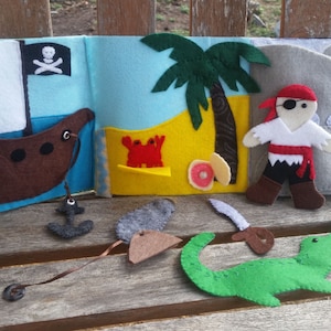 May include: A felt book for children with a pirate ship, a palm tree, a pirate, a crocodile, and a crab. The book is made of felt and has a variety of textures.