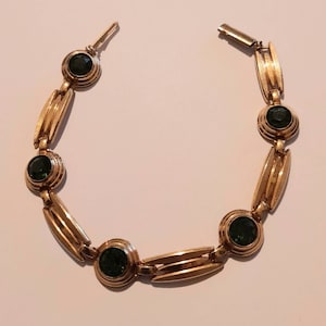 May include: A gold bracelet with five green gemstones. The bracelet has a clasp closure.