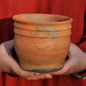 Può includere: Un vaso in terracotta fatto a mano con una smaltatura marrone rustica e un design ondulato intorno al centro. Il vaso è leggermente più largo nella parte superiore rispetto alla parte inferiore.