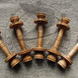 Pode incluir: Seis devanadores de fio de madeira com um acabamento liso de cor castanho claro. Os devanadores têm um design simples com um eixo central e dois discos circulares em cada extremidade.