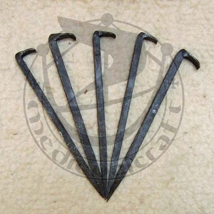 May include: Five dark metal pry bars arranged in a fan shape. Each bar has a curved, hooked end and a long, straight shaft. The tools appear to be made of iron or steel, with a slightly weathered appearance. The background is a light, textured surface.