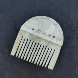 May include: A white bone comb with a rounded top and decorative circles. The comb has 17 teeth and is approximately 4 inches long.