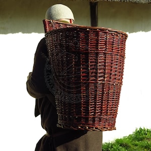 Może przedstawiać: Osoba w brązowej szacie nosi na plecach duży, wiklinowy kosz w kolorze czerwono-brązowym.