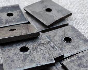 Peut inclure: Une pile de rondelles carrées en métal avec un trou au centre. Les rondelles sont de couleur gris foncé et ont une texture rugueuse.