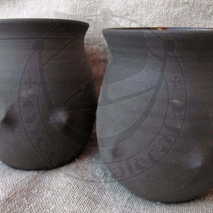 Può includere: Due vasi in ceramica grigio scuro con corpo arrotondato e bordo svasato. Ogni vaso presenta una caratteristica protuberanza a forma di capezzolo sul lato. I vasi sono esposti su una superficie strutturata grigio chiaro.