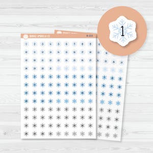 May include: Sheets of snowflake-shaped stickers with numbers 1-31. The stickers are in shades of blue and gray, with a white background. The stickers are from Orange Umbrella Co.