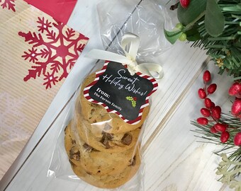 May include: A clear cellophane bag tied with a cream ribbon, containing chocolate chip cookies. A black tag with red and white trim reads "Sweet Holiday Wishes!" and "From: The Farson Family." A red and white snowflake gift bag is in the background.