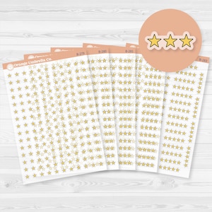 May include: Several sheets of stickers with gold star designs. The stickers are arranged in rows and columns on white backgrounds. The brand name "Orange Umbrella Co." is visible on one sheet. A circular graphic with three gold stars is also present.