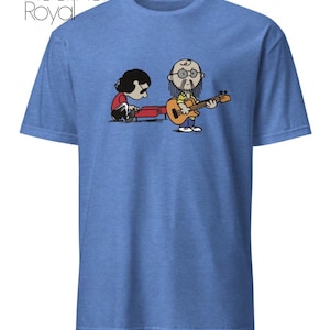 May include: A heather royal blue short-sleeve t-shirt featuring a graphic print of two cartoon characters playing music. One character plays a red piano while the other plays a yellow guitar. The text "Heather Royal" is printed in the top left corner.
