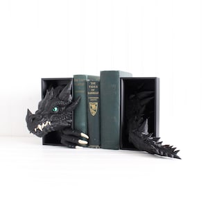 May include: Black dragon bookends with a detailed head and tail design. The dragon's head has a green eye and white fangs. The bookends are holding up several green books.