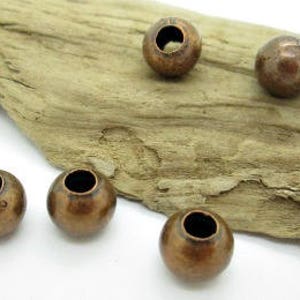 May include: Five antique copper-colored metal beads with a hole in the center. The beads are round and have a slightly textured surface.