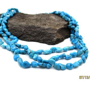 May include: A multi-strand necklace composed of numerous small, polished, bright blue turquoise-colored stone chips. The necklace is arranged in loose, overlapping loops, showcasing the irregular, tumbled shapes of the individual stones.