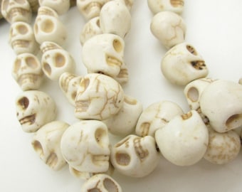 May include: A strand of white skull beads. The beads are made of bone or ceramic and have a detailed skull design.