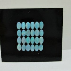 May include: A collection of 16 oval-shaped blue opal cabochons, arranged in a grid pattern on a black background.
