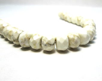May include: A strand of faceted, off-white beads featuring irregular tan and brown veining throughout each piece. The beads are arranged in a curved line, showcasing a polished, multi-faceted surface that reflects light across their textured, stone-like appearance.