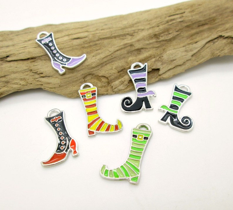 May include: Six silver witch boot charms with different colored stripes and designs. The charms are on a wooden surface.