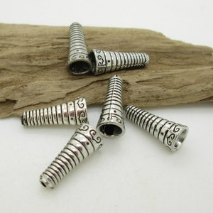 May include: Five silver metal cone-shaped beads with decorative etched designs. The beads are approximately 1 inch long.