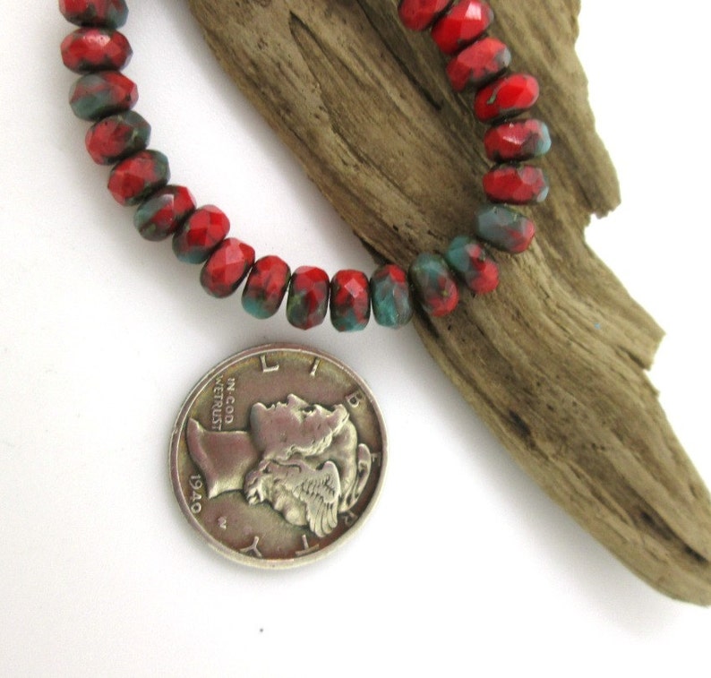 May include: A strand of faceted beads in red and teal hues. The beads are displayed next to a silver coin from 1940 and a piece of driftwood. The beads are approximately 0.25 inches in diameter.