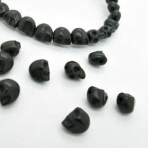 May include: A strand of black skull beads, with additional loose beads scattered around. The beads are made of a smooth, matte material.