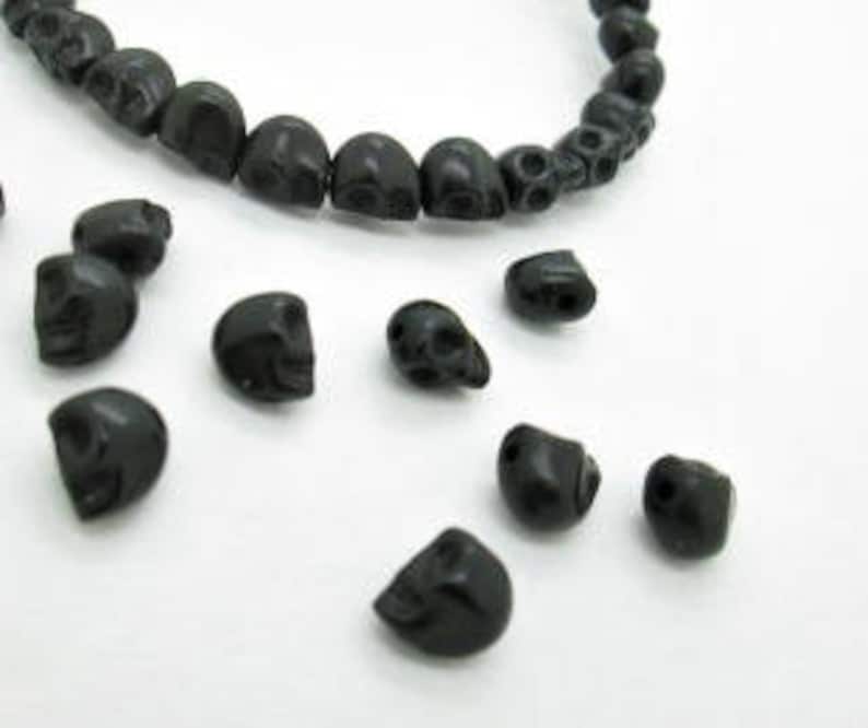 May include: A strand of black skull beads, with additional loose beads scattered around. The beads are made of a smooth, matte material.