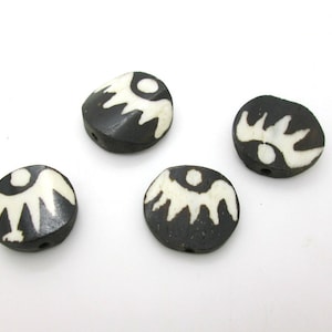 May include: Four black and white round beads with a white design of stylized wings and a circle. The beads have a hole through the center for stringing.