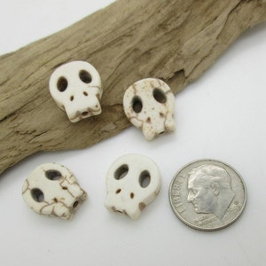 May include: Four white skull beads with brown markings, next to a US dime for size comparison.