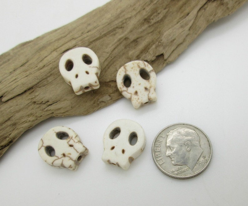 May include: Four white skull beads with brown markings, next to a US dime for size comparison.