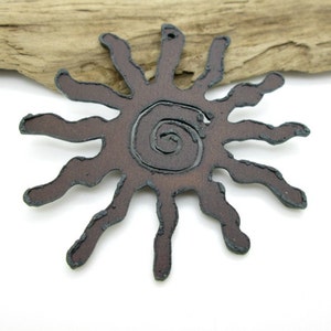 May include: A brown metal sun with a spiral design in the center. The sun has 12 rays and is a rustic, hand-crafted style.