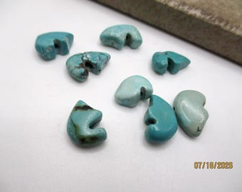 May include: A collection of eight turquoise beads with irregular, curved shapes and side-drilled holes. The beads display varying shades of blue and green, with some featuring dark brown matrix veining. The date 07/18/2026 is printed in yellow.