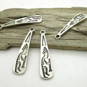 May include: Four silver-toned metal charms with a Kokopelli design. Two charms are teardrop-shaped, and two are rectangular. The charms are displayed on a piece of weathered wood.