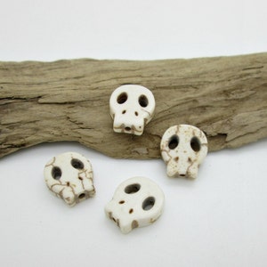 May include: Four white skull-shaped beads with brown markings. The beads are made of natural stone and have a smooth, polished finish.