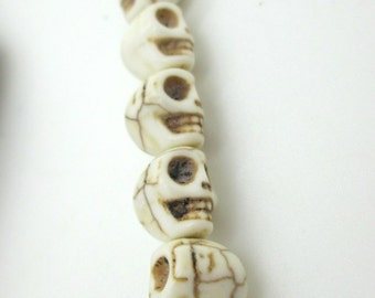 May include: A strand of off-white skull beads with brown detailing. The beads are strung together, creating a unique and edgy accessory. The skulls have detailed facial features and a cracked texture.