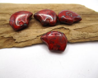May include: Four red, teardrop-shaped beads with a speckled, glossy finish. The beads are arranged on a piece of weathered wood against a white background. The beads have a dark red base colour with hints of blue and black.