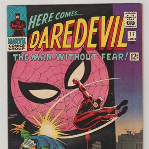 K&ouml;nnte beinhalten: Vintage Comic-Cover mit Daredevil in einer dynamischen Actionpose. Das Cover hat einen rosa Spinnennetz-Hintergrund mit dem Titel "DAREDEVIL" in gro&szlig;en gelben Buchstaben. Der Text "The Man Without Fear" ist ebenfalls sichtbar.