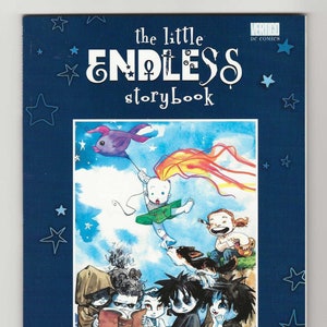 Op de afbeelding: Een blauwe boekomslag met de titel "The Little Endless Storybook" in wit en zwart schrift. De omslag toont een kleurrijke illustratie van een baby die een vlieger met een vis erop vliegt, en een groep kinderen die op een heuvel zitten. Het boek is van Jill Thompson.
