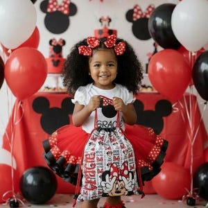 K&ouml;nnte beinhalten: Ein l&auml;chelndes Kind h&auml;lt einen Minnie Mouse-Kordelzugbeutel. Sie tr&auml;gt einen rot-schwarzen T&uuml;llrock, ein wei&szlig;es Oberteil und schwarze Turnschuhe. Rote, wei&szlig;e und schwarze Luftballons und Dekorationen schaffen eine festliche Atmosph&auml;re.