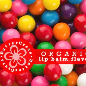 May include: A close-up of a variety of colorful gumballs. The gumballs are arranged in a random pattern and are all the same size. The gumballs are surrounded by a red banner with the text "ORGANIC lip balm flavor" in white letters. The banner is also surrounded by a red circle with a white flower design and the text "ButterCress.ButterCress" in white letters.