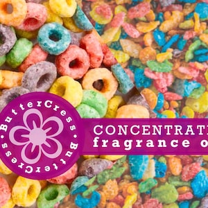 Könnte beinhalten: Nahaufnahme von bunten Cerealienstücken, mit einem rosafarbenen Kreislogo, auf dem "ButterCress" in weißer Schrift steht. Der Text "CONCENTRATED fragrance oil" ist in weißer Schrift auf einem violetten Hintergrund.