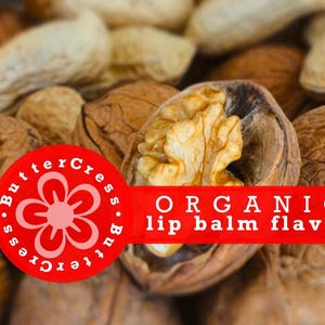 Puede incluir: Primer plano de nueces y cacahuetes. Una nuez está abierta, revelando la nuez. Un círculo rojo con un gráfico de flores y las palabras "ButterCress" rodea la flor. Una pancarta roja dice "ORGANIC lip balm flavor."