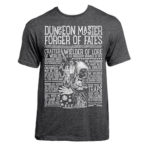 Op de afbeelding: Een donkergrijs t-shirt met een wit grafisch ontwerp. Het ontwerp bevat een schedel, dobbelstenen en tekst die luidt "Dungeon Master Forger of Fates, Crafter Wielder of Lore of Worlds & An Unhealthy Number of Dice, Encounters May Be Fun But See Me Scorn By Player's Yawn & I Can Summon More, Behind My Screen All Secrets Lie But Test My Wrath Then Say Goodbye, Roll With Me To Gain XP I'll Do The Rest, The Mastermind of Many Tales & Endless Fleshed Out NPC's, The Weaver of Minute Details From Ancient Rumes To Tavern Cheese, There Might Be Traps There Might Be Treasure But My Greatest Role Is To Ensure Players Roll", Het grafische ontwerp doet denken aan een vintage poster.