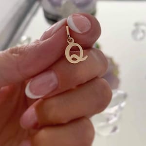 Puede incluir: Un peque&ntilde;o colgante de metal en tono dorado pulido con forma de letra may&uacute;scula Q. El colgante presenta una superficie lisa y reflectante y una peque&ntilde;a anilla circular en la parte superior para engancharlo a una cadena, de dise&ntilde;o simple.