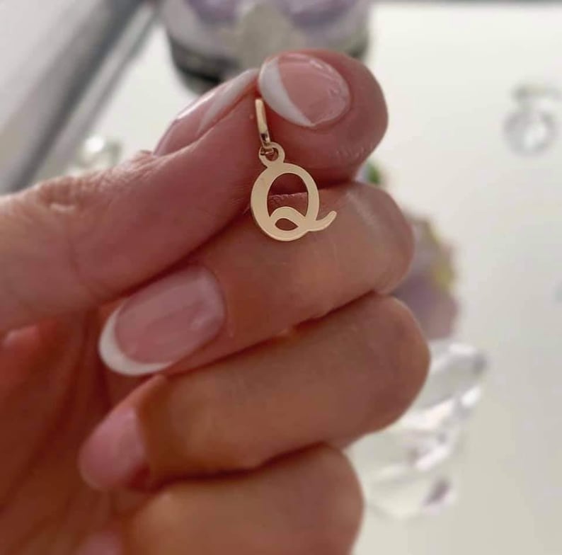 Puede incluir: Un peque&ntilde;o colgante de metal en tono dorado pulido con forma de letra may&uacute;scula Q. El colgante presenta una superficie lisa y reflectante y una peque&ntilde;a anilla circular en la parte superior para engancharlo a una cadena, de dise&ntilde;o simple.