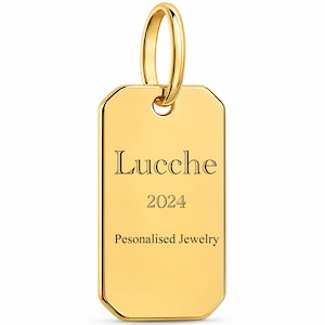 Peut inclure: Un pendentif rectangulaire doré poli aux coins arrondis, surmonté d'une bélière circulaire. La face avant porte l'inscription gravée "Lucche", l'année "2024" et la mention "Pesonalised Jewelry" dans une police à empattement sombre et nette.