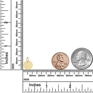 Puede incluir: Un peque&ntilde;o colgante redondo de color dorado con un lazo para una cadena. El colgante tiene aproximadamente 1,3 cm de di&aacute;metro. Una regla con pulgadas y mil&iacute;metros est&aacute; en el fondo, junto con un centavo y un cuarto de d&oacute;lar para la comparaci&oacute;n de tama&ntilde;os.